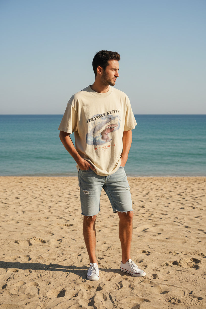 Beige t-shirt with graphic design and text on a hanger indoors