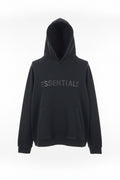 Folded black hoodie with 'ESSENTIALS' text on a patterned surface