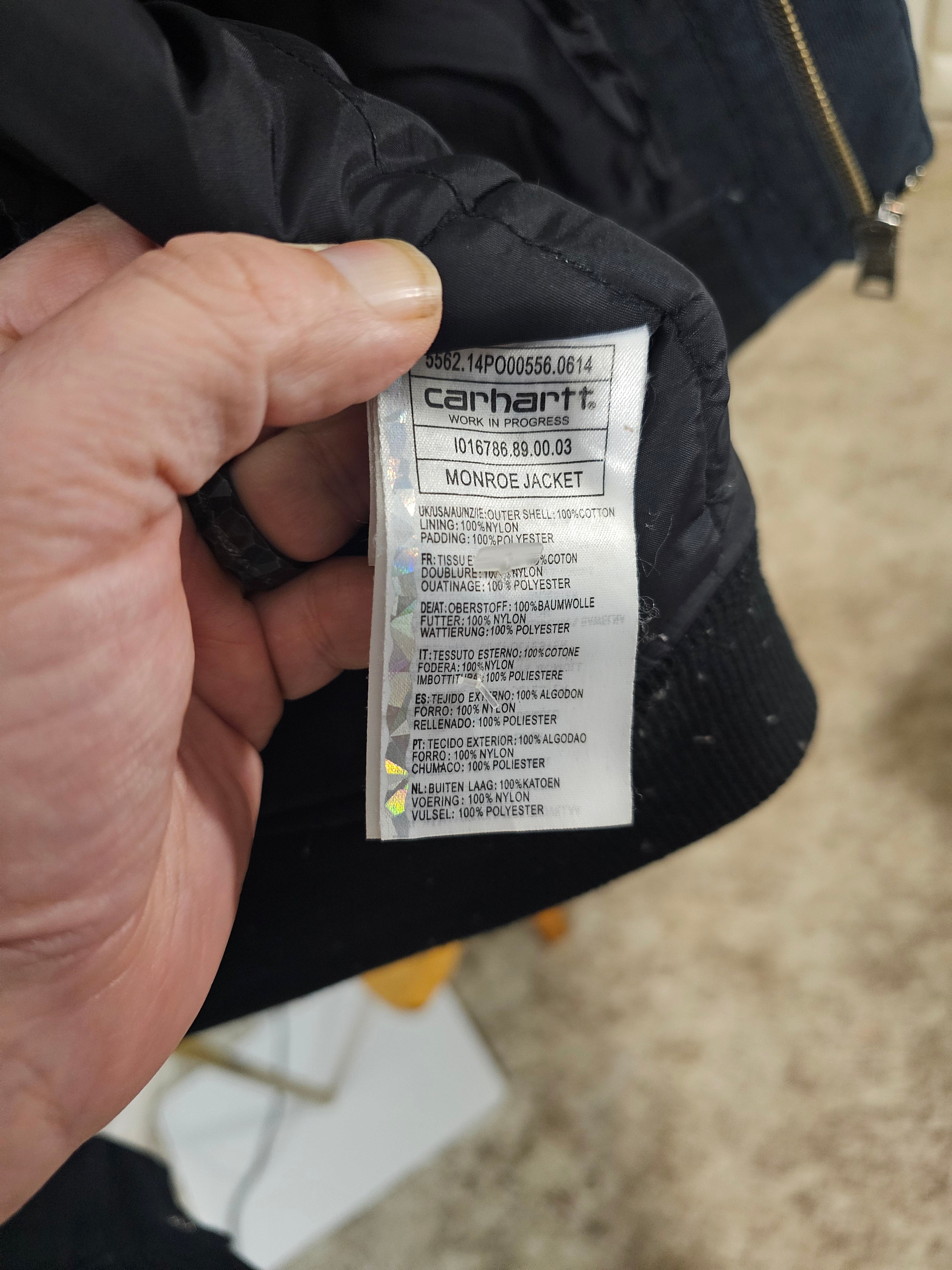 Hand holding a Carhartt label on a black jacket against a blurred background
